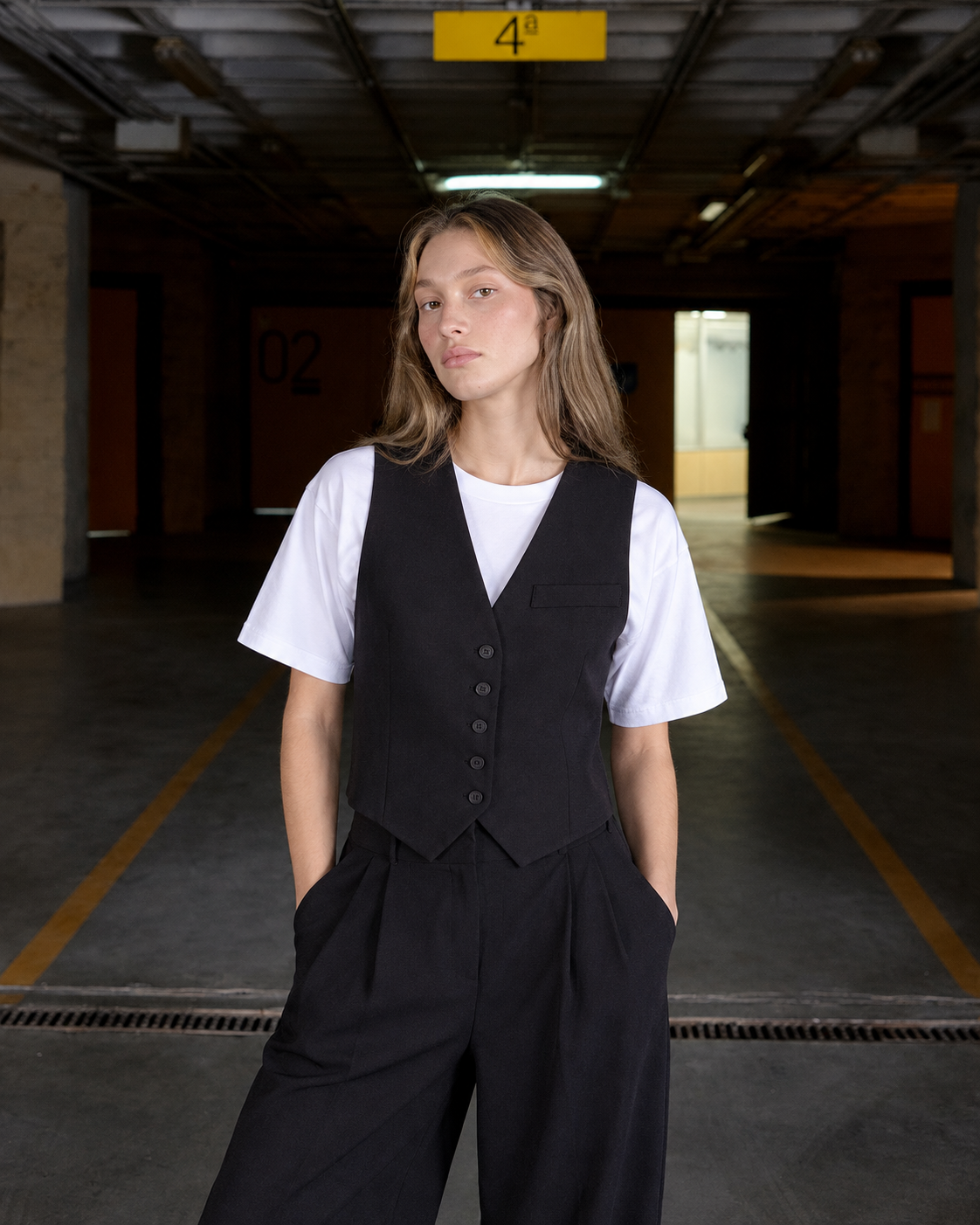 Modelo de frente con camiseta ARLO blanca, chaleco negro MISIA y pantalón ancho negro